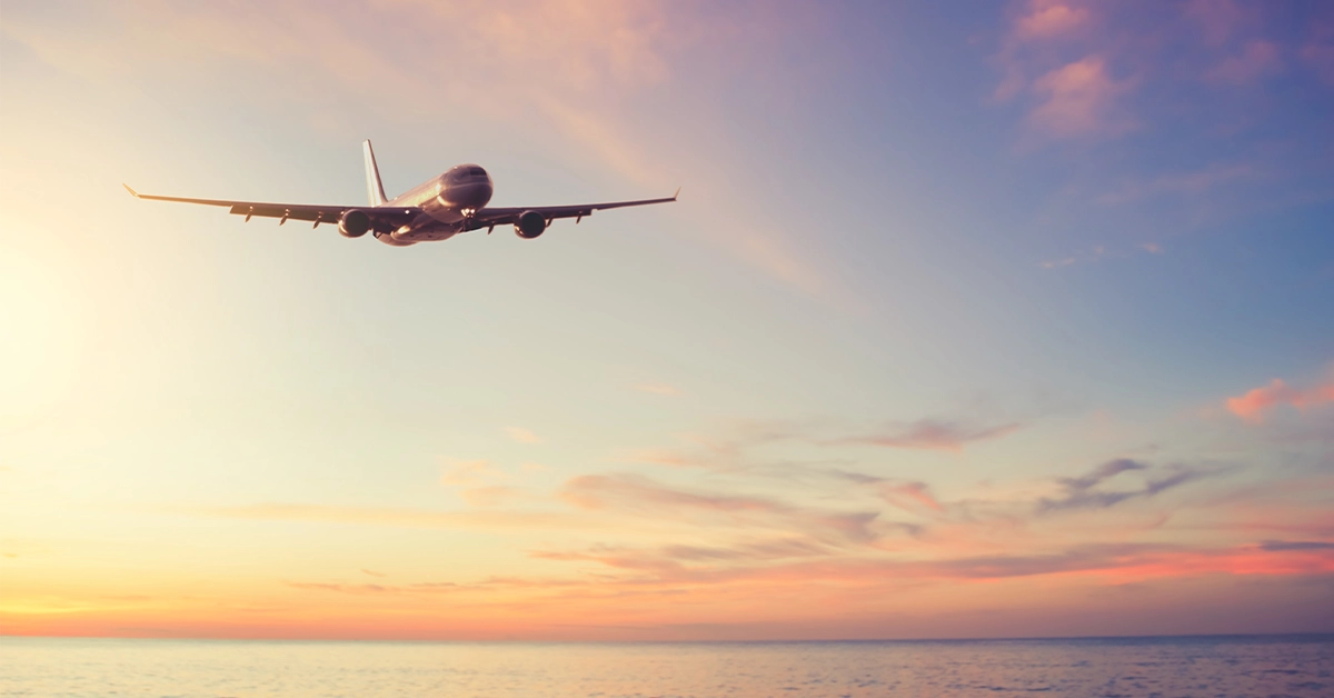 Passenger airplane flying above the ocean at sunset representing air travel to Florida’s Treasure Coast
