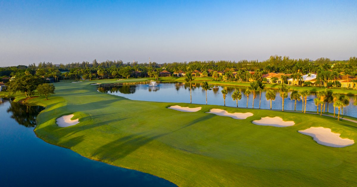 Aerial view of a luxury golf course community with pristine greens, sand bunkers, and waterfront homes surrounding a scenic lake.