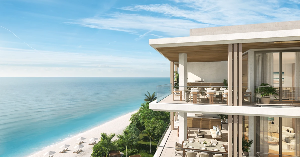 Modern oceanfront residence with glass balconies overlooking a sandy beach and calm blue water.